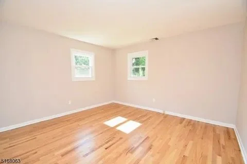 Empty room with two windows, light-colored walls, and hardwood flooring.