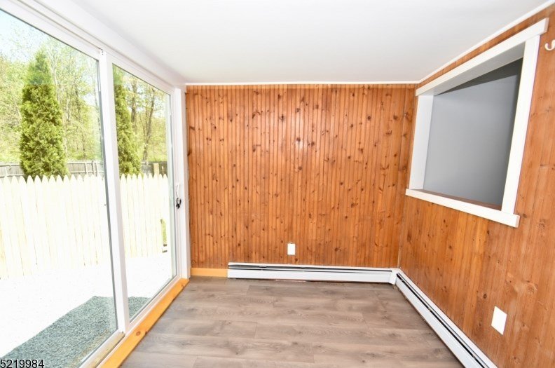 Empty room with wood-paneled wall, a large sliding glass door to the outside, a small rectangular window, and flooring that looks like laminate.