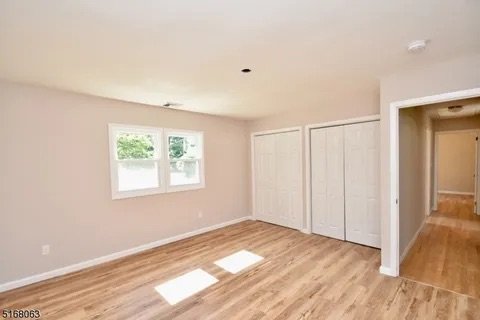 Empty room with light-colored walls, hardwood floors, a window with green trees outside, and white closet doors.