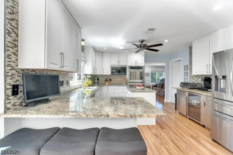 Modern kitchen with white cabinets, granite countertops, stainless steel appliances, a small TV, and a ceiling fan, open to a living area with a sofa.