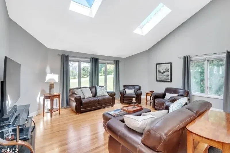 Bright living room with large windows, skylights, and leather sofas.