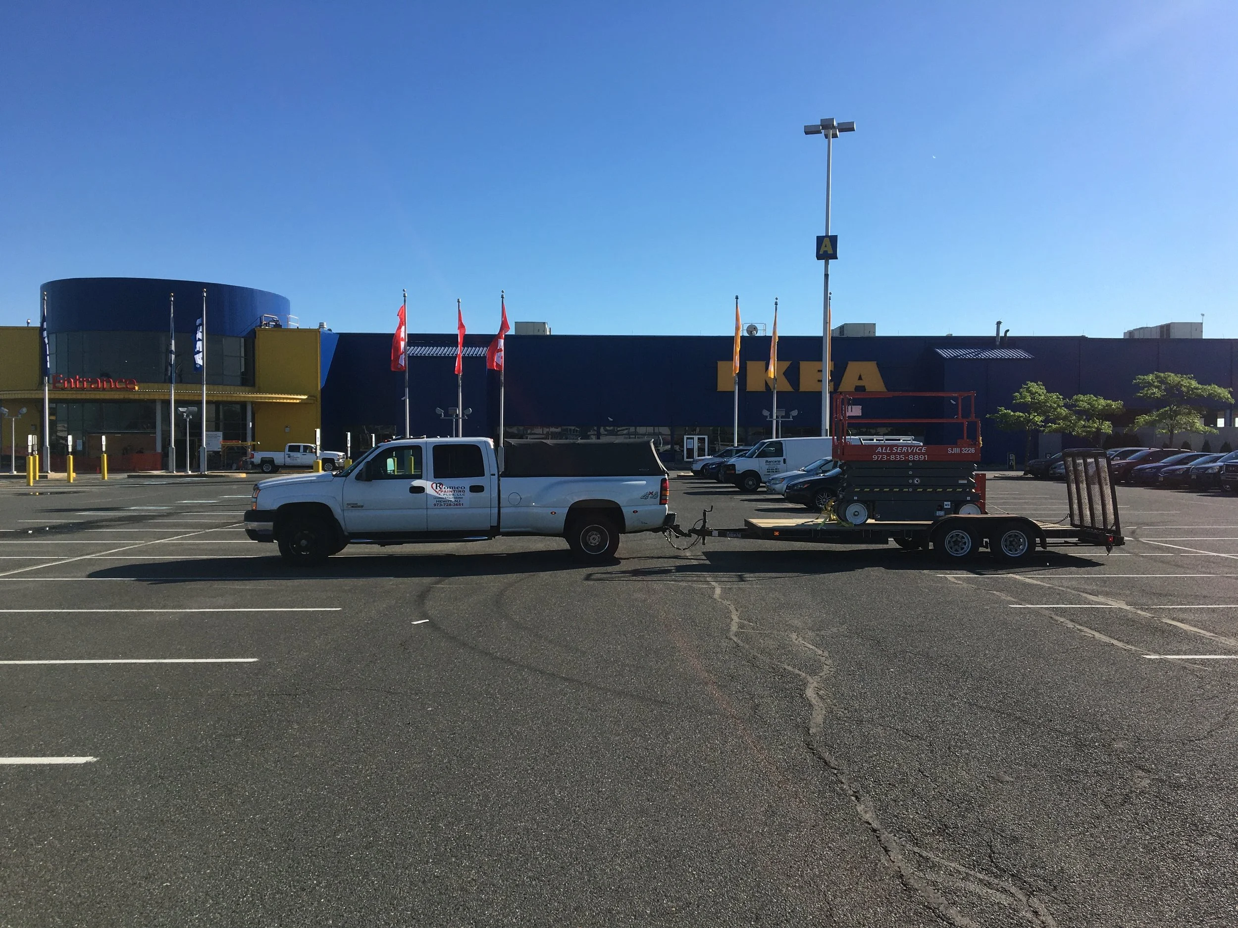 Parking lot outside IKEA store with white pickup truck towing a trailer and a scissor lift.