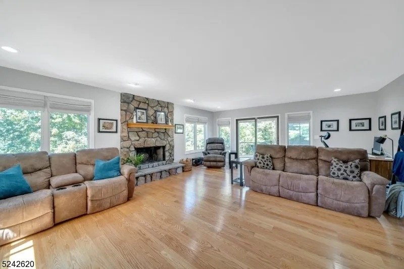 Living room with two beige sofas, a stone fireplace, a rocking chair, framed pictures on the walls, and hardwood flooring.
