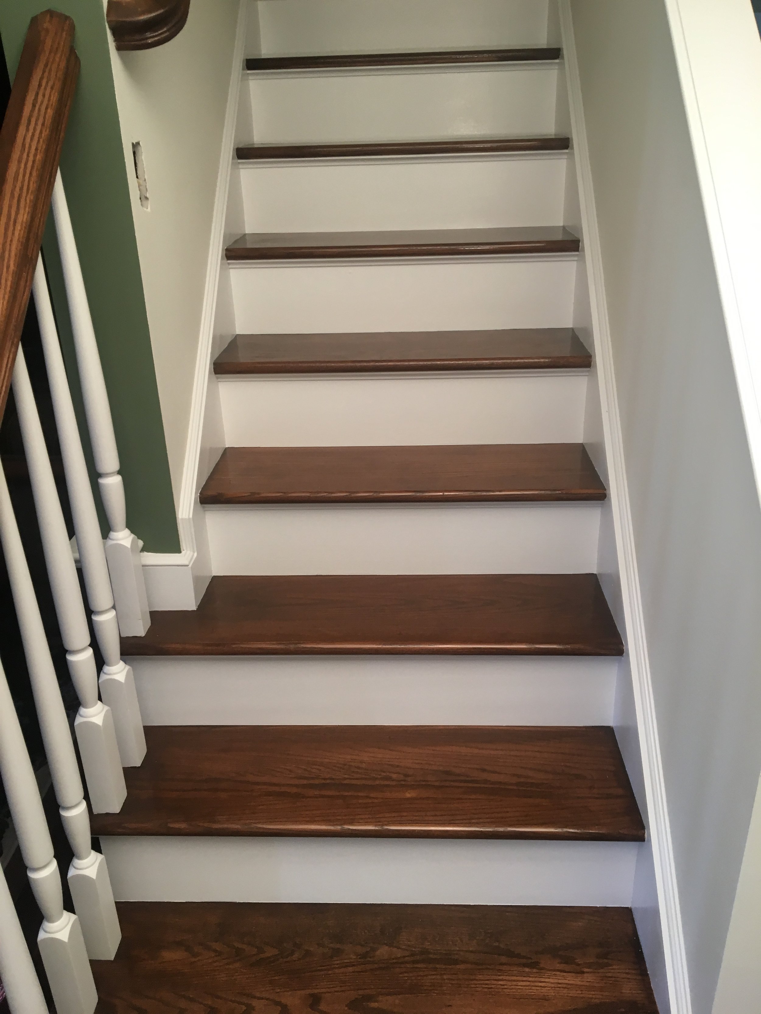 Photo of a staircase with dark wood steps and white risers, with a green wall and white railing on the side.
