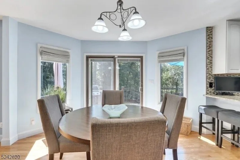 Dining area with a round wooden table and four upholstered chairs in a bright kitchen with windows and a sliding glass door.