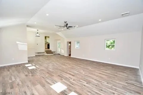 Empty living room with hardwood floors, white walls, ceiling fan, and multiple windows allowing natural light.