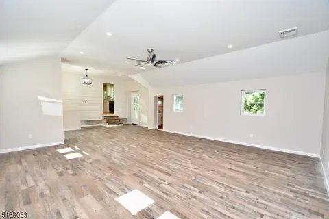 Empty living room with white walls, wood flooring, ceiling fan, and recessed lighting.