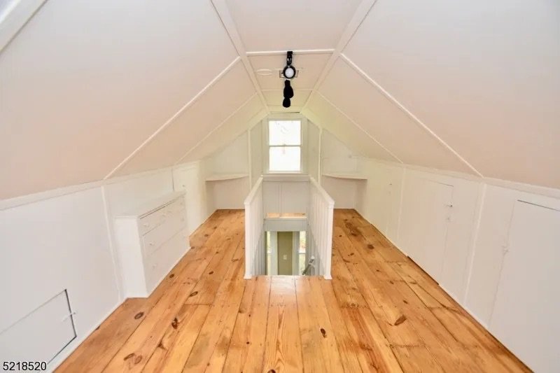Small attic with white walls, sloped ceiling, wooden floor, small window, central staircase, and a hanging rope with a bell or pulley.
