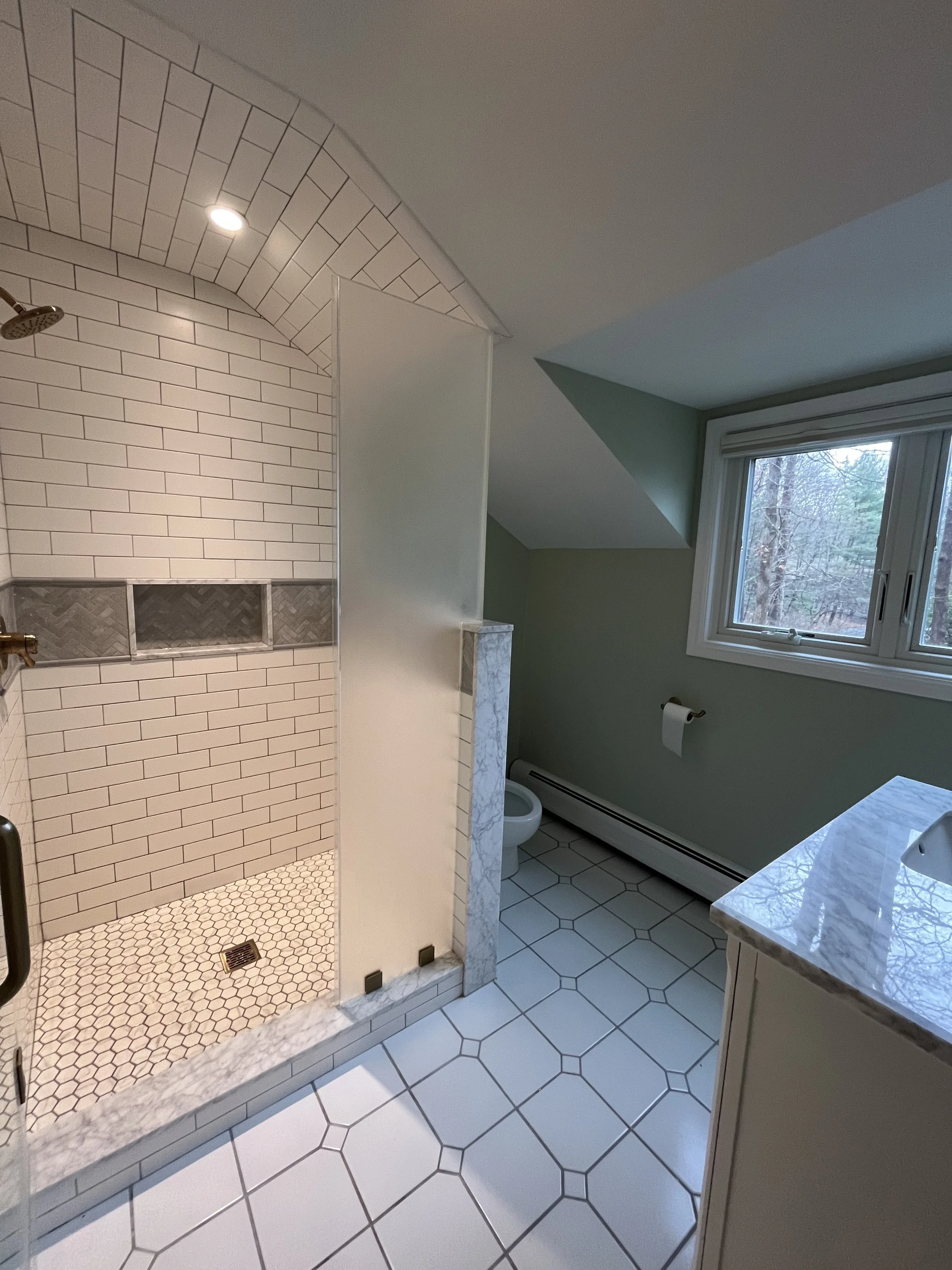 Bathroom with walk-in shower, white subway tile, hexagonal floor tiles, window, vanity with marble countertop, toilet, and a green wall.