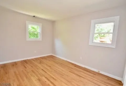 Empty room with two windows, white walls, and hardwood floor.