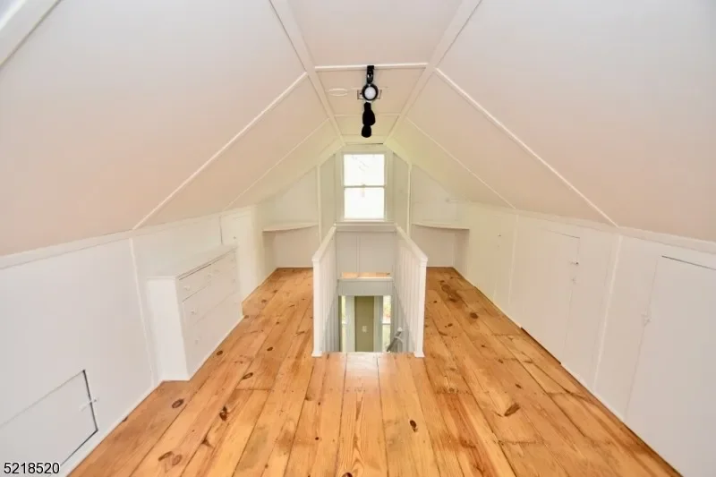 Empty attic space with white paneled walls, a small window, and wooden floor, with a staircase at the far end leading down.