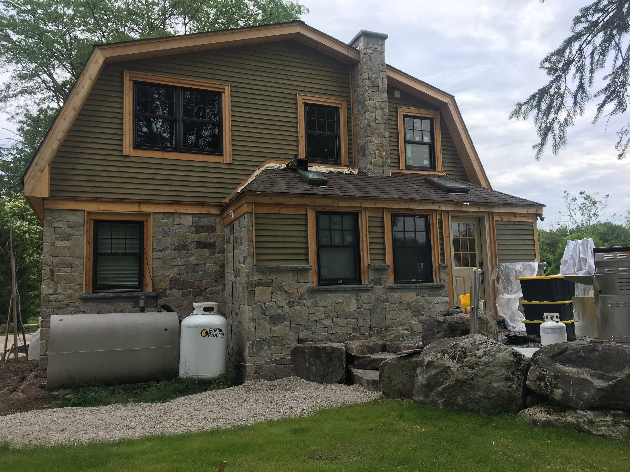 A two-story house under construction with stone and siding exterior, multiple windows, a chimney, and construction materials and tools outside.