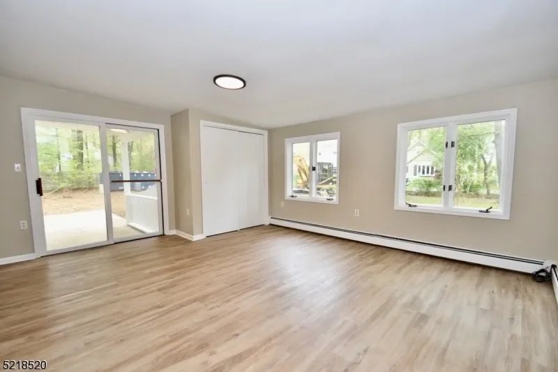 Empty living room with hardwood floors, white walls, multiple windows, a sliding glass door leading to an outdoor patio, and a ceiling light fixture.