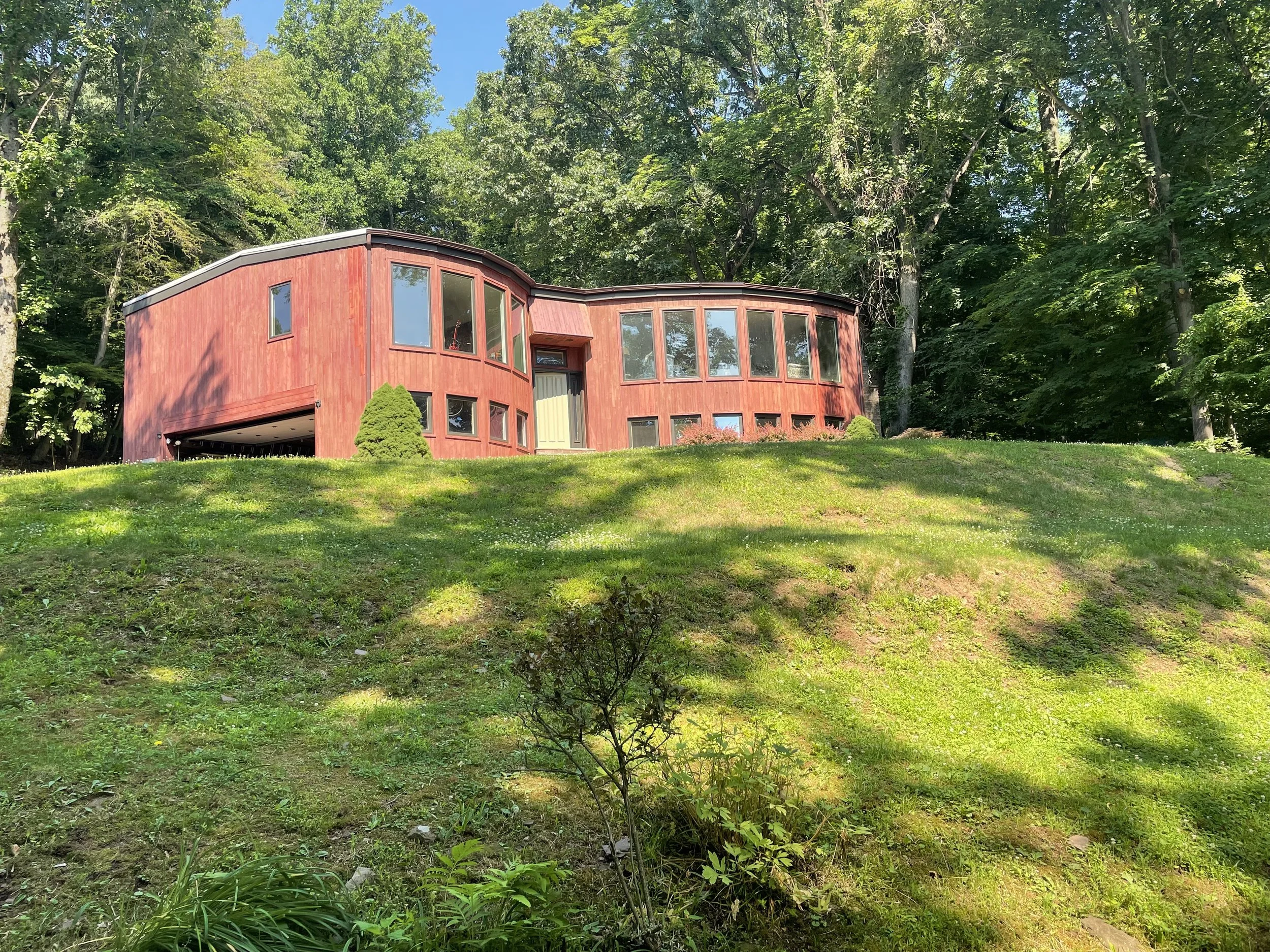 Red house with large windows on a grassy hill surrounded by trees.