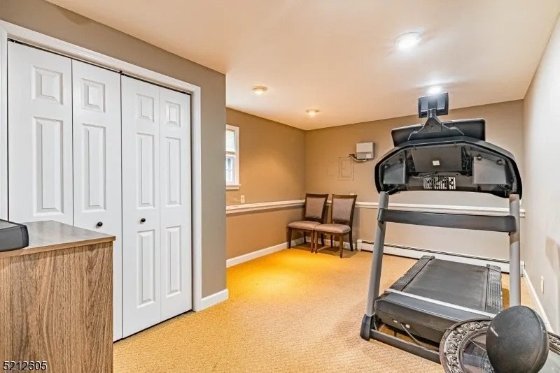 A small room with beige walls and carpet, contains two chairs, a treadmill, and a small cabinet.