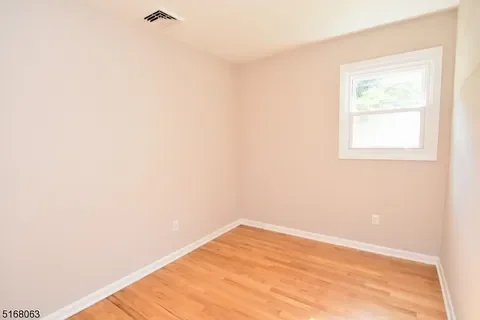 Empty room with beige walls, a window, and hardwood flooring.