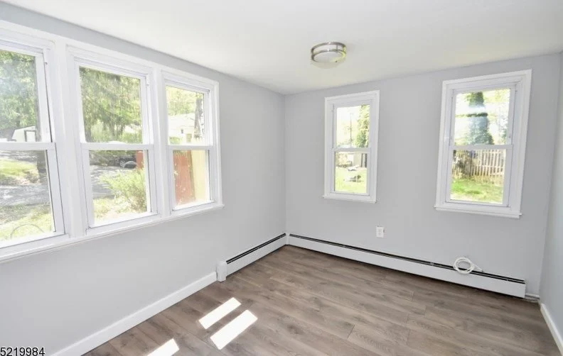 Empty room with light gray walls, hardwood floor, and large windows letting in natural light.