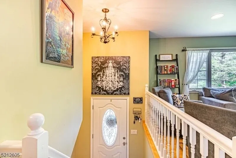 View of a home interior entrance and living room with green and yellow walls, decorated with artworks, chandelier, bookshelf, and window with curtains.