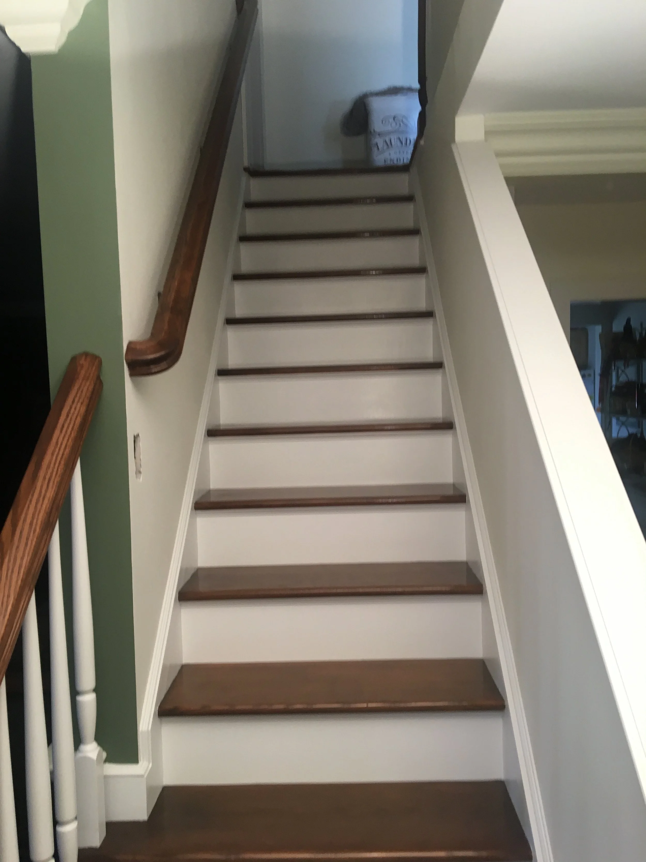 Indoor staircase with wooden steps, white risers, with a green wall on the left and a stair railing with wooden handrail.