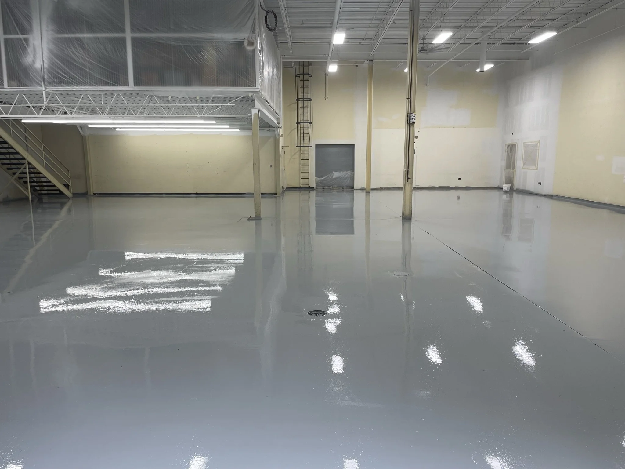 Empty interior space with a highly reflective gray floor, yellow walls, ceiling lights, and structural support beams.