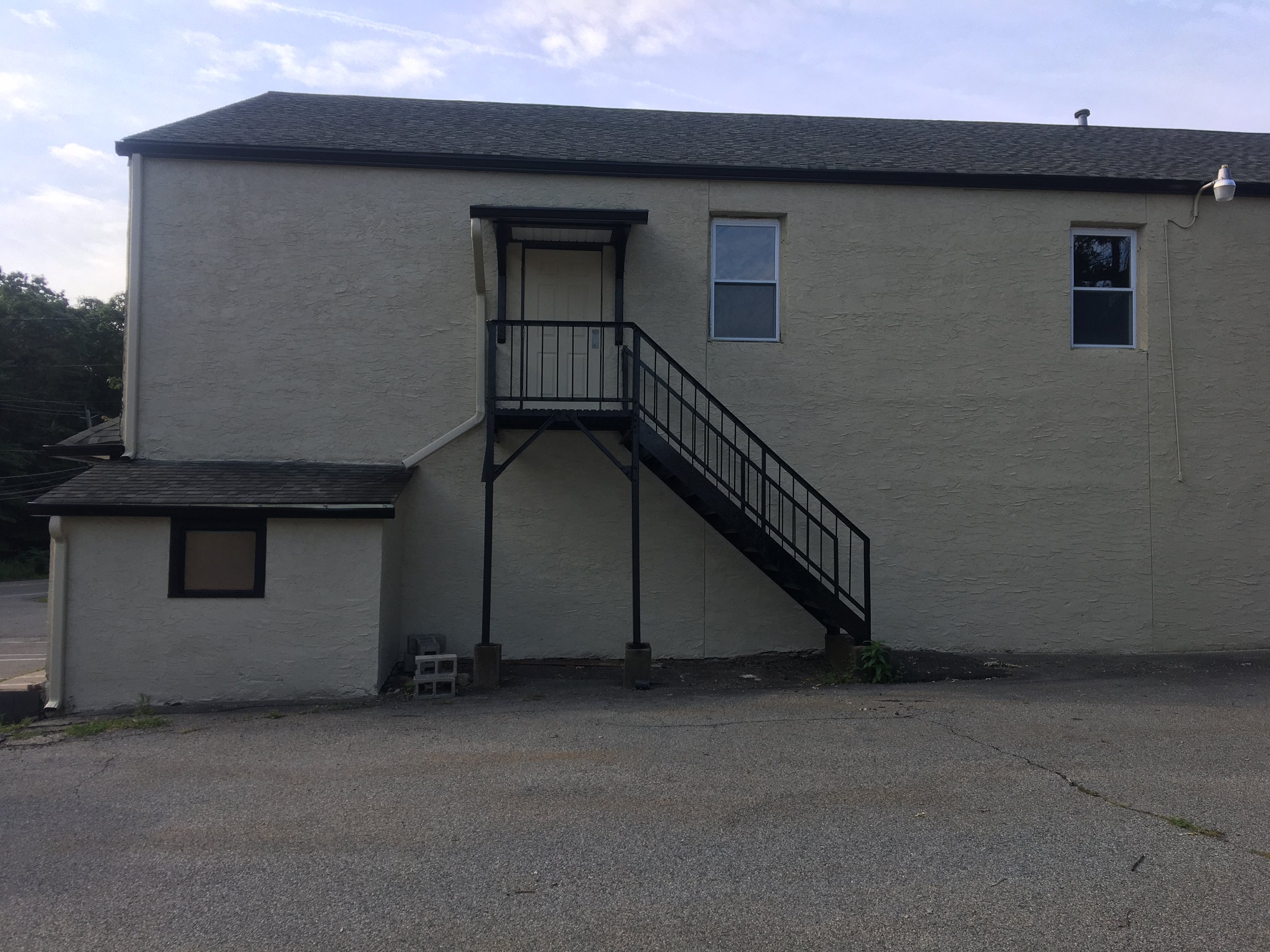 The back of a two-story beige building with a black staircase leading to a door on the second floor.