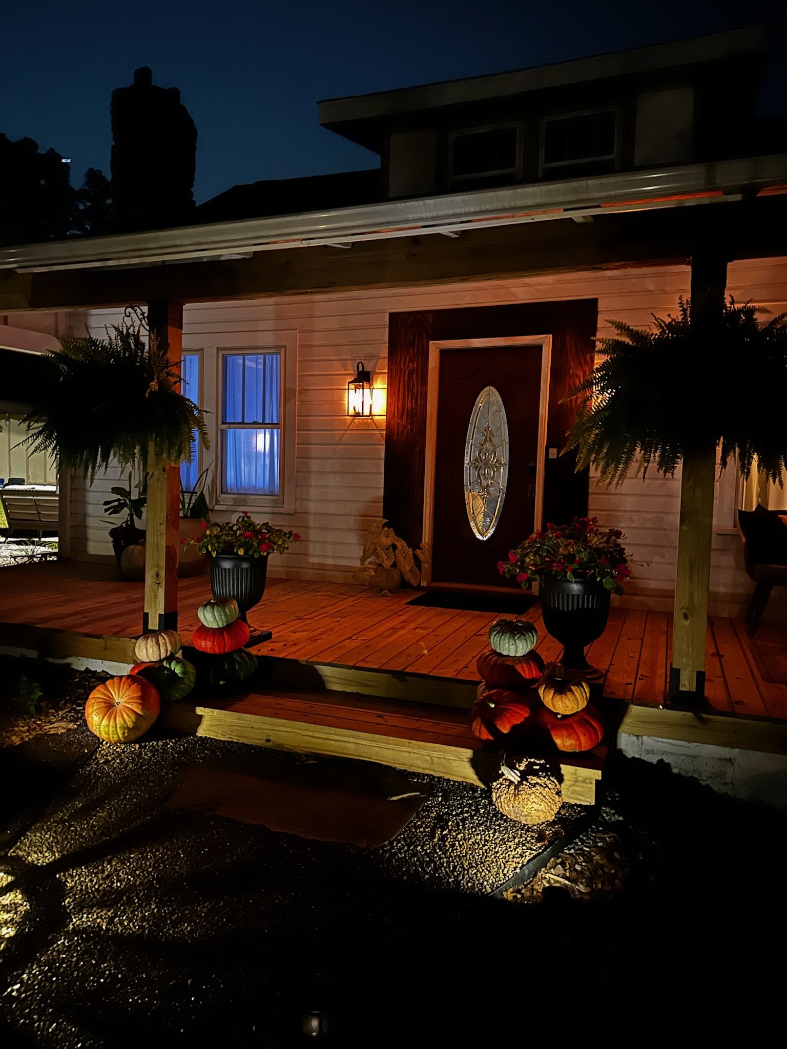 Exterior of a house at night decorated with pumpkins and potted plants on the porch.