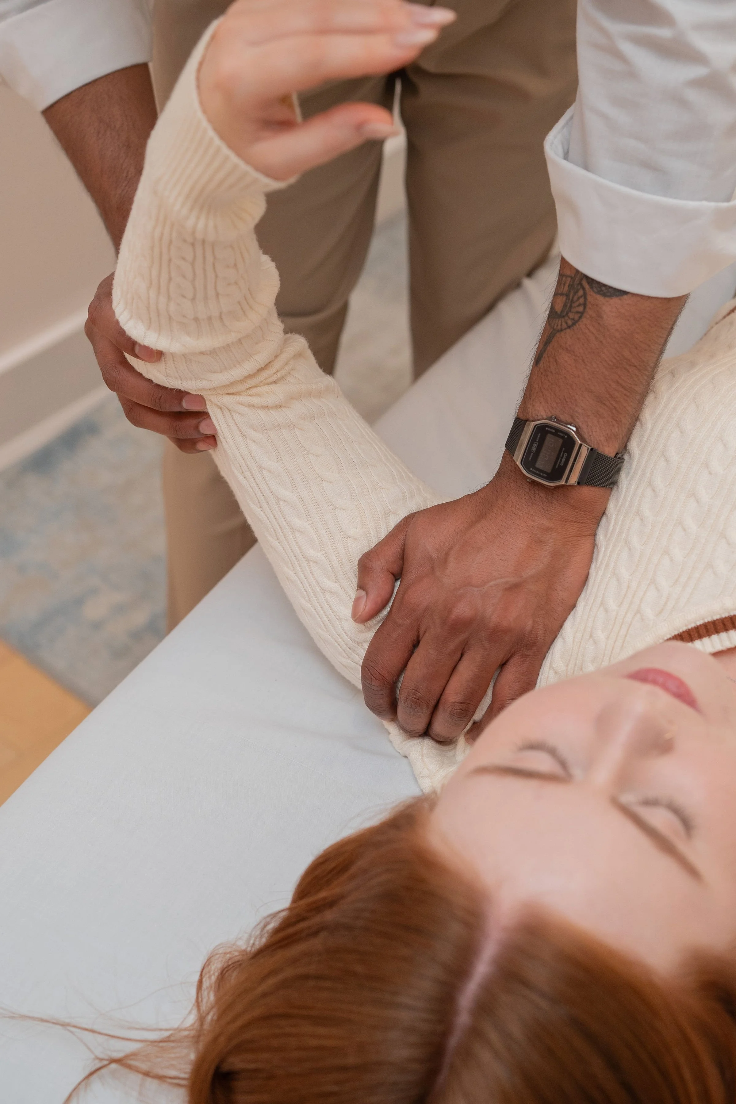 A person receiving a physical therapy or massage treatment while lying on a table, with someone supporting their arm and inserting a device into their hand