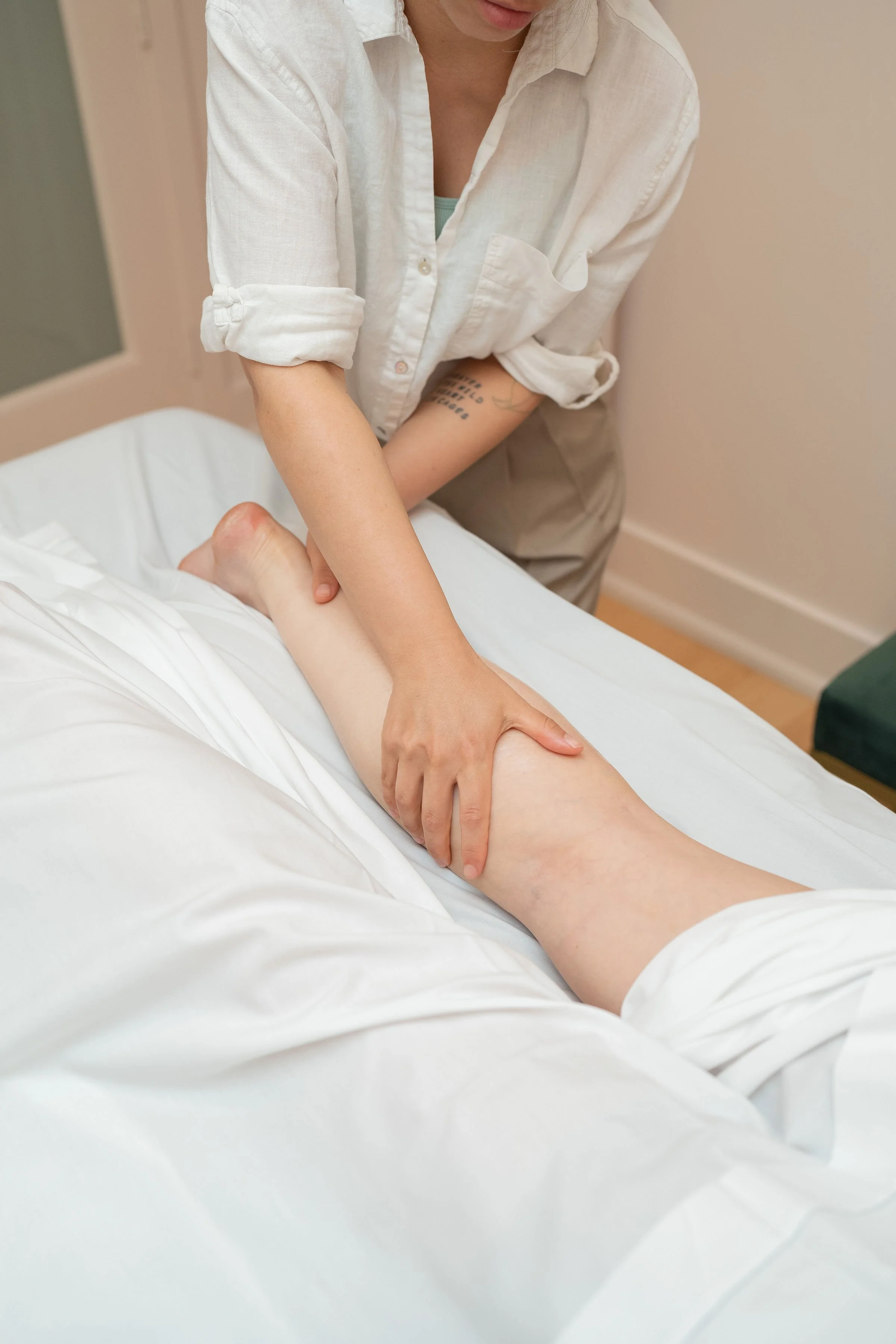 A person giving a leg massage to someone lying on a bed, with the focus on the hand on the lower leg.