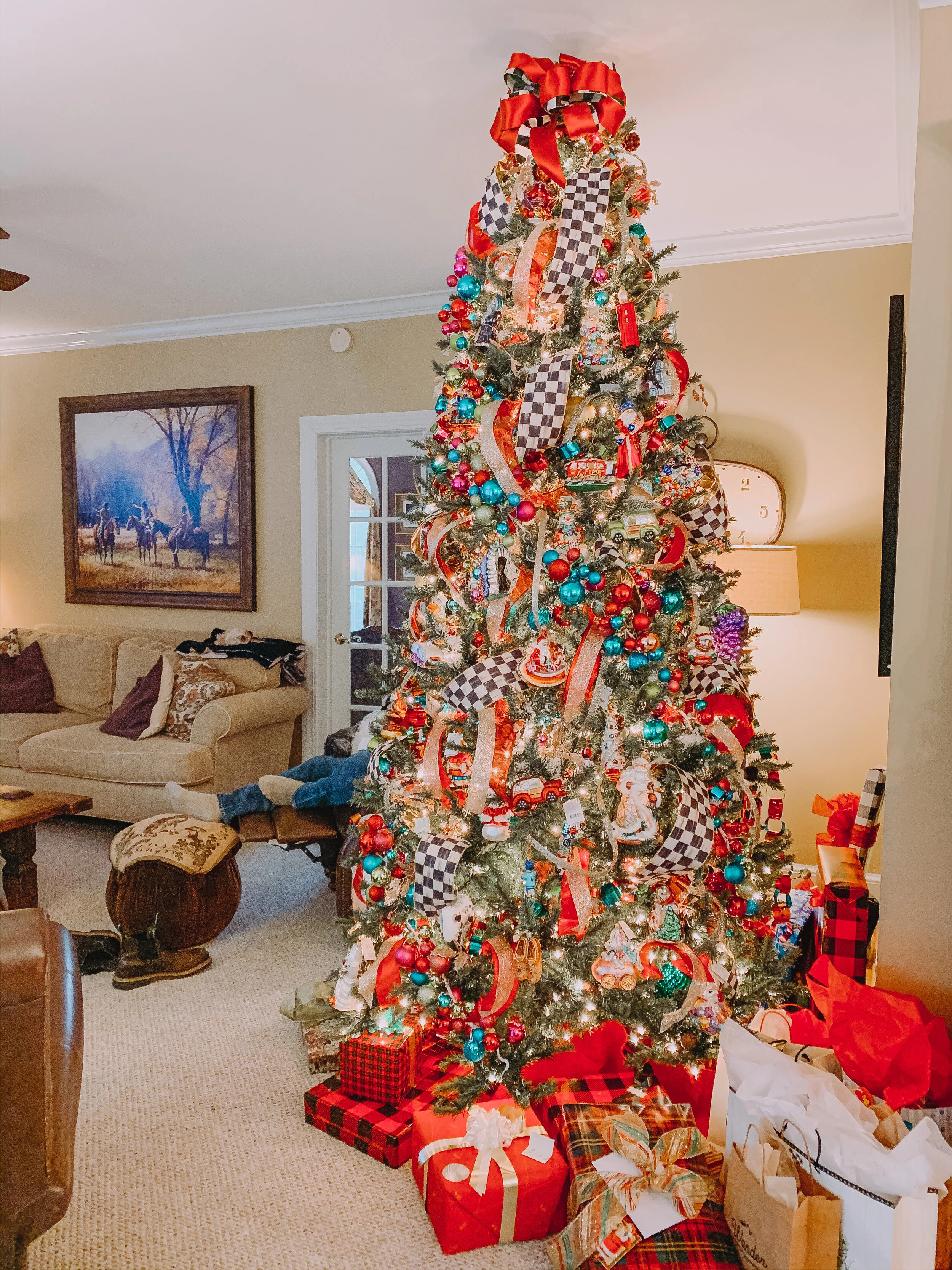 Decorated Christmas tree with ornaments, ribbons, and presents underneath in a living room.