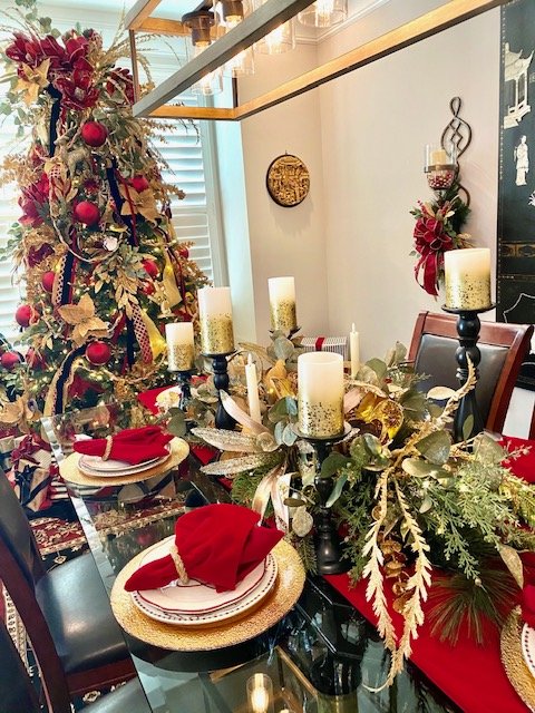 Christmas decorated dining table with candles, greenery, and red napkins, with a Christmas tree in the background