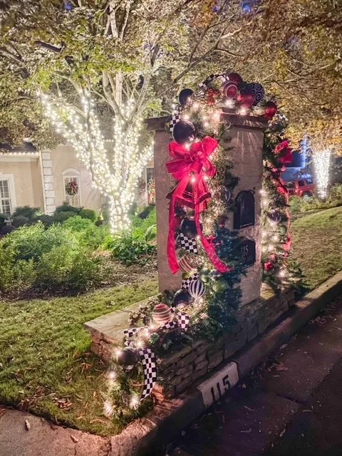 Decorated fireplace with Christmas garland, lights, and a big red bow on a sidewalk at night.