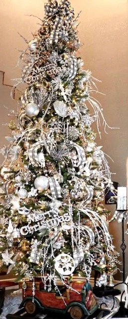 A tall Christmas tree decorated with silver and white ornaments, ribbons, and garlands in a festive indoor setting.