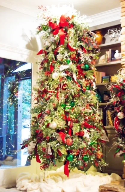 Decorated Christmas tree with red ribbons, ornaments, and lights in a festive room.