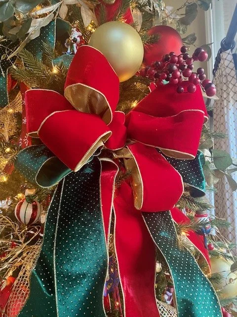 Close-up of a decorated Christmas tree with a large red and green bow, gold and red ornaments, and red berries.
