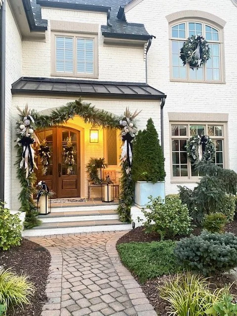 Decorated front porch with Christmas wreaths and garland on a white house during holiday season.