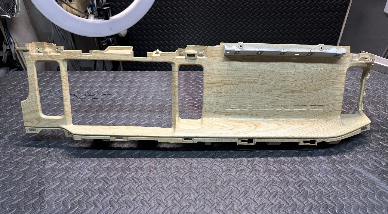 Wooden and metal parts of a dashboard frame on a textured surface.