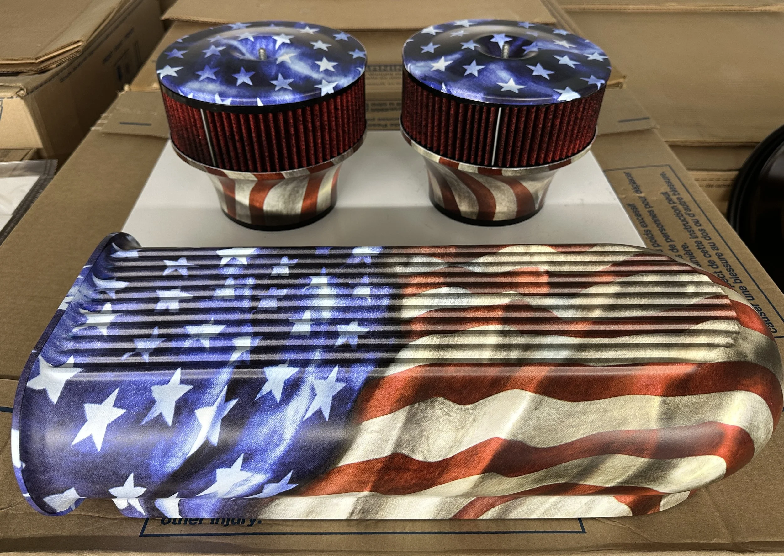 Two circular automotive air filters with stars and stripes design sitting on a white surface, with one large decorative tray featuring a matching American flag design in front of them.