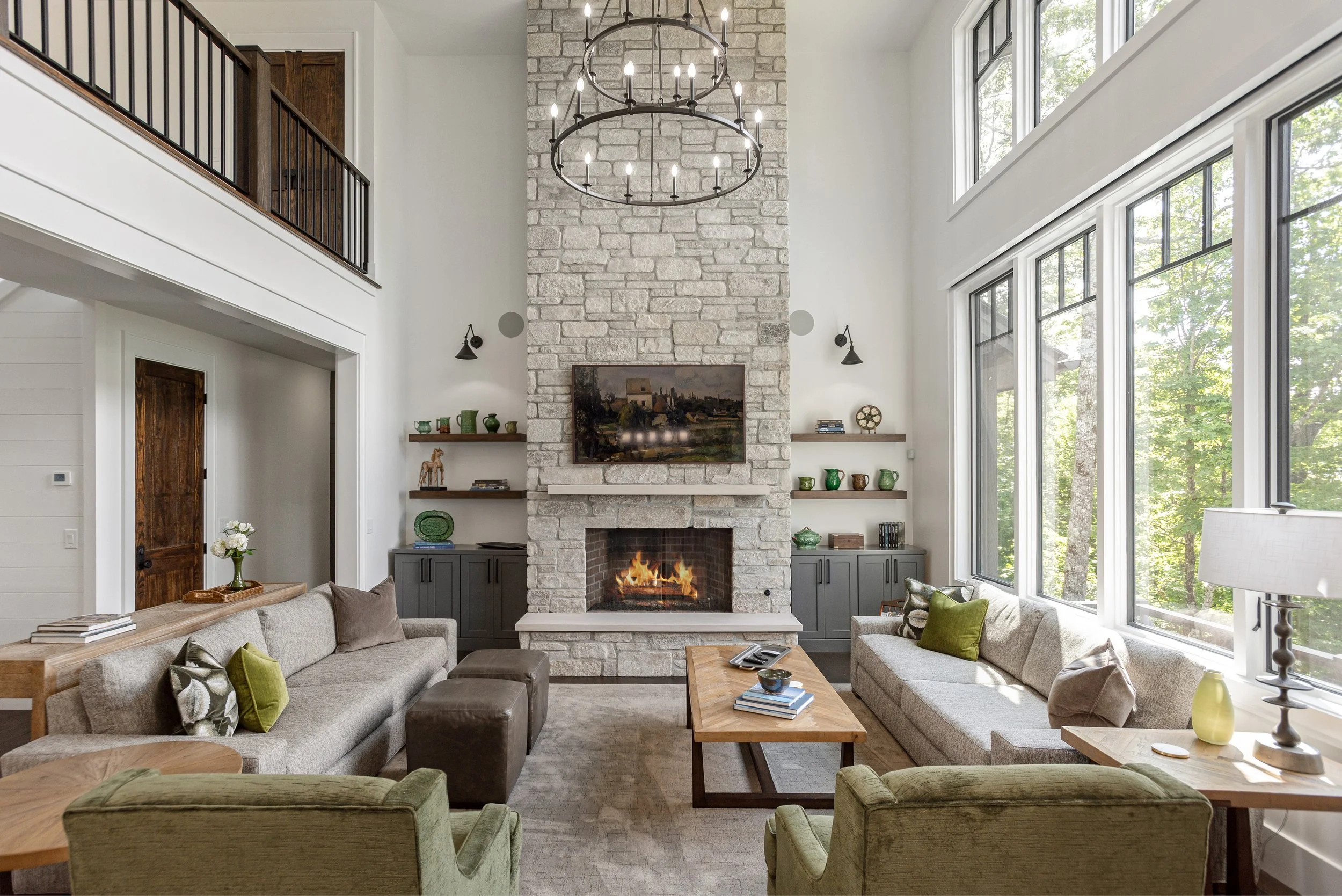Living room with a stone fireplace, large windows, and modern decor including sofas, armchairs, and wooden tables.
