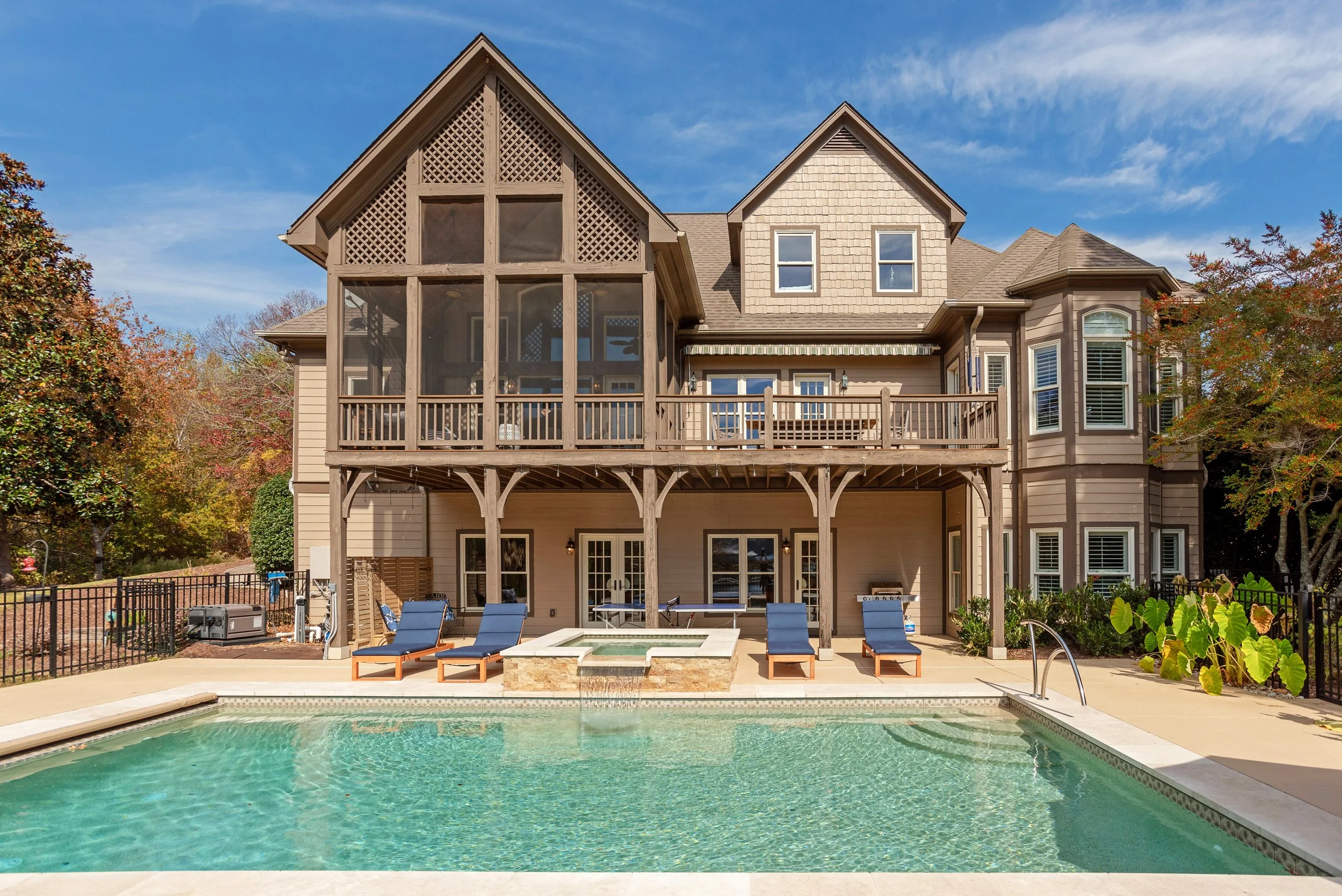 The image shows the backyard of a house with a swimming pool, poolside chairs, a hot tub, and a large multi-story house with a deck and screened porch.