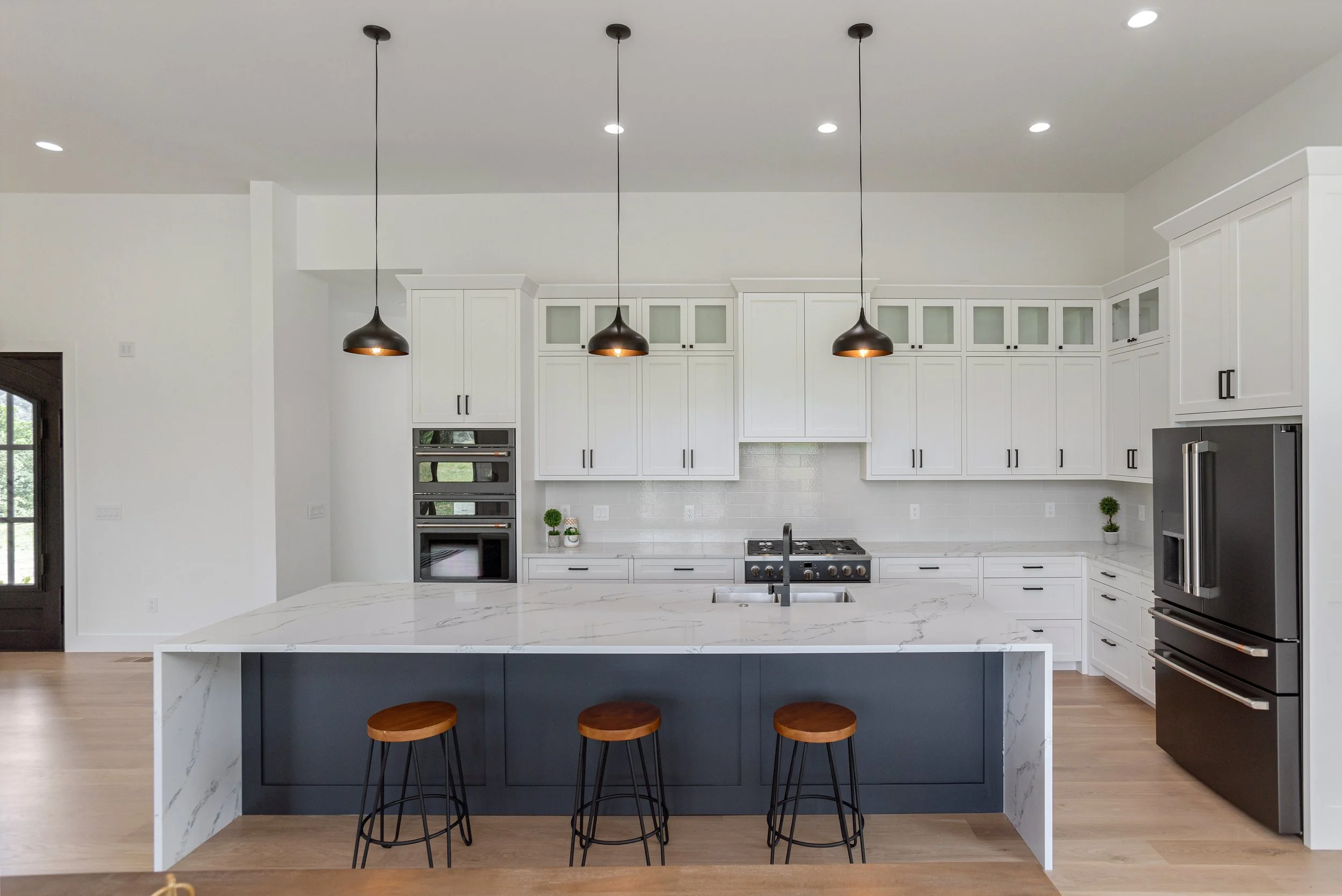 Modern kitchen with white cabinets, black pendant lights, marble island, and stainless steel appliances.