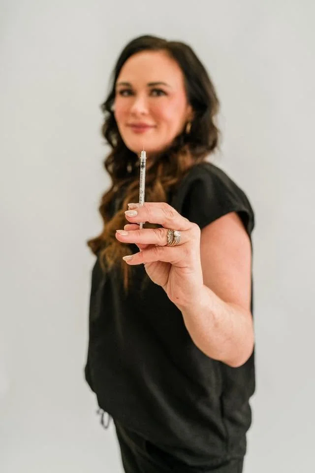 Dr Heather Lawson holding a syringe and smiling, wearing a black top