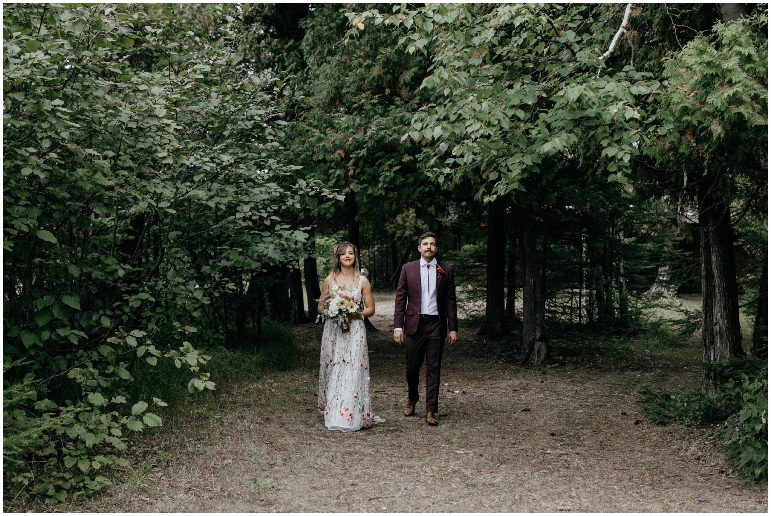 Bride and groom walking together during ceremony processional at summer camp wedding on half moon lake in Eveleth Minnesota