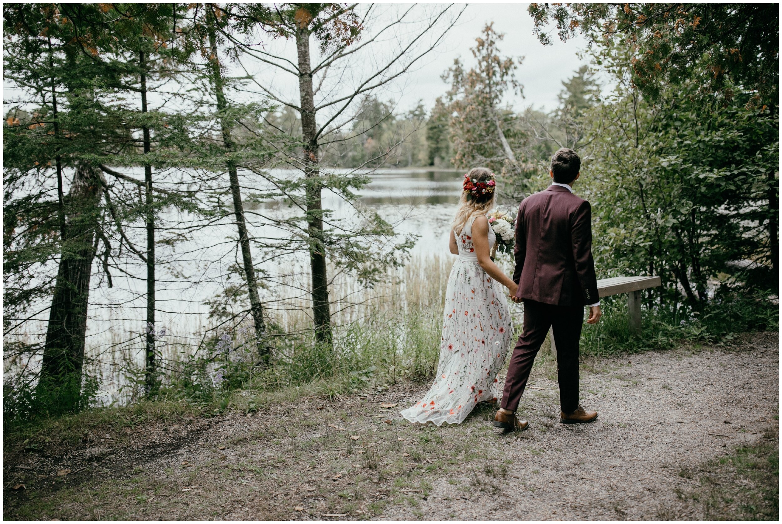 Bride and groom walking past half moon lake in northern Minnesota after whimsical wooded summer camp wedding