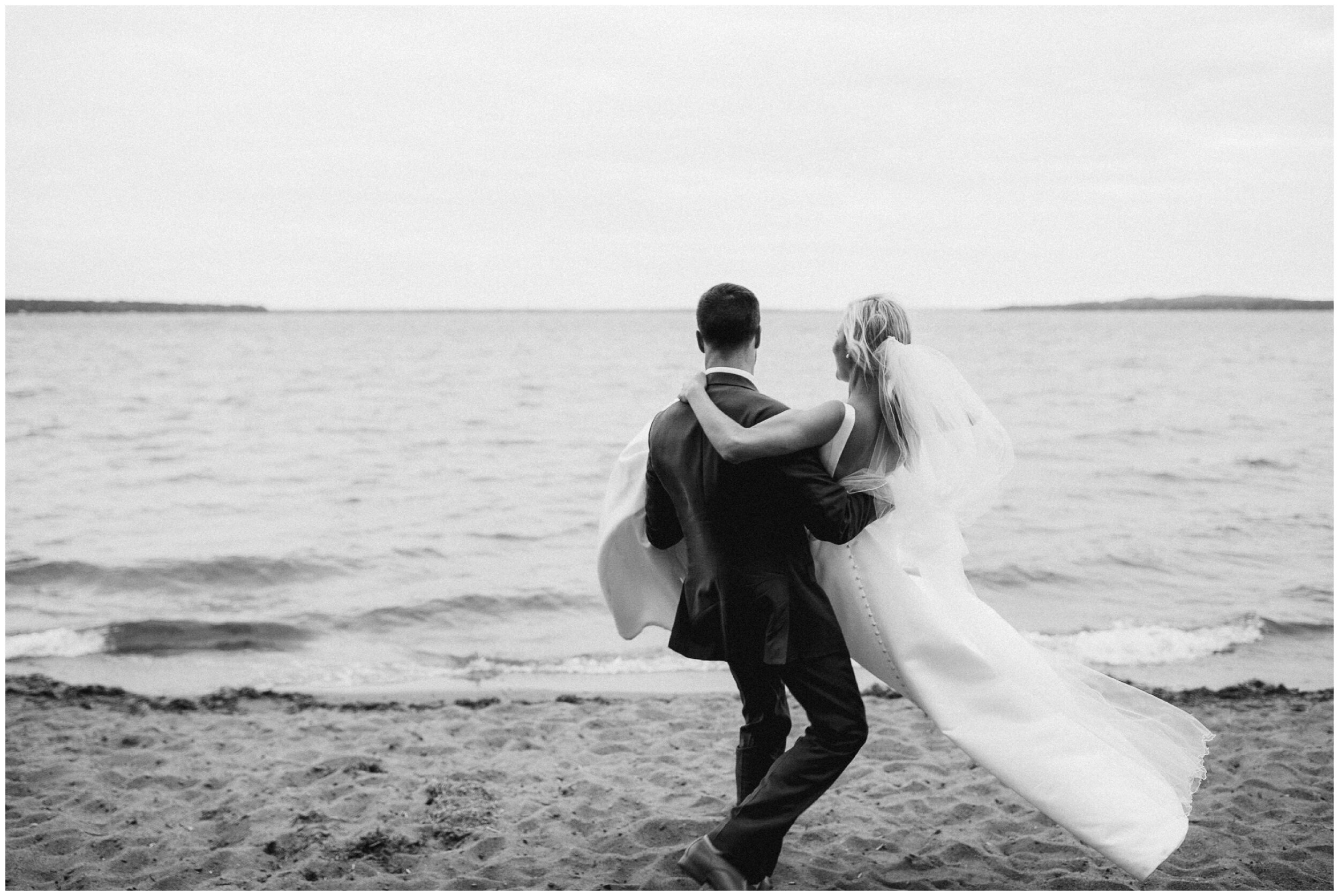 Groom carrying bride on gull lake beach at grand view lodge wedding in nisswa minnesota