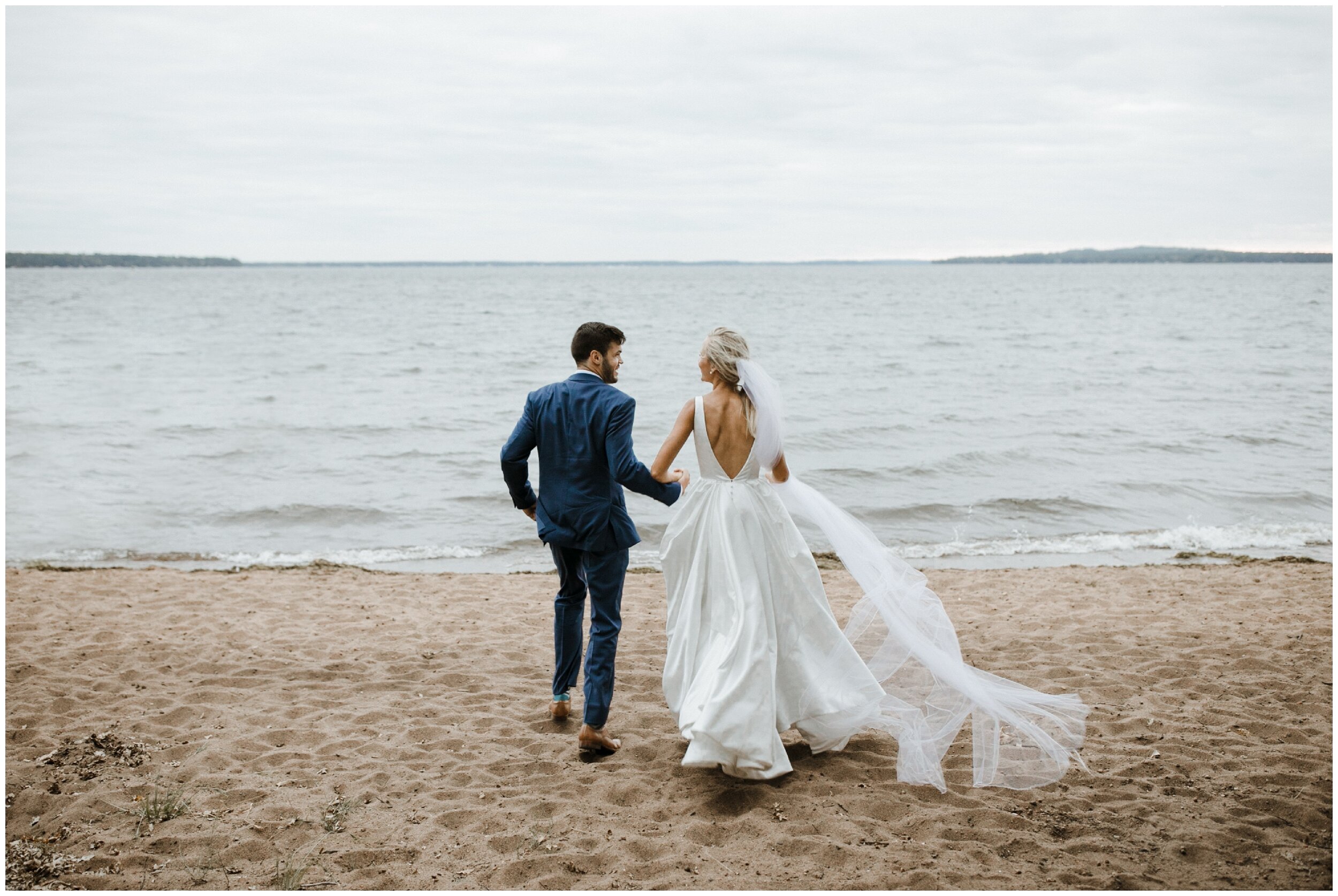 Bride and groom running on sandy beach on gull lake at luxury Grand View Lodge wedding