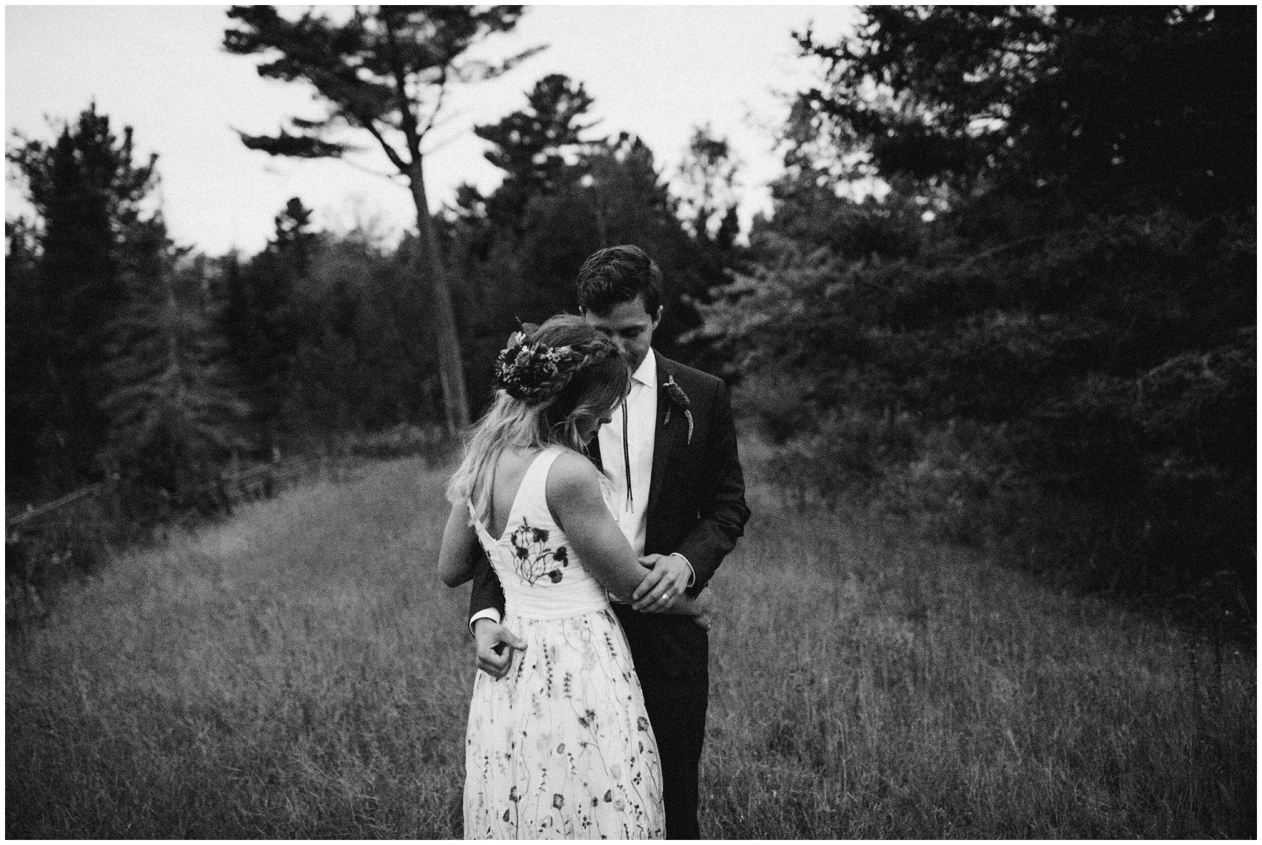 Bride and groom standing in field surrounded by woods at Minnesota summer camp wedding