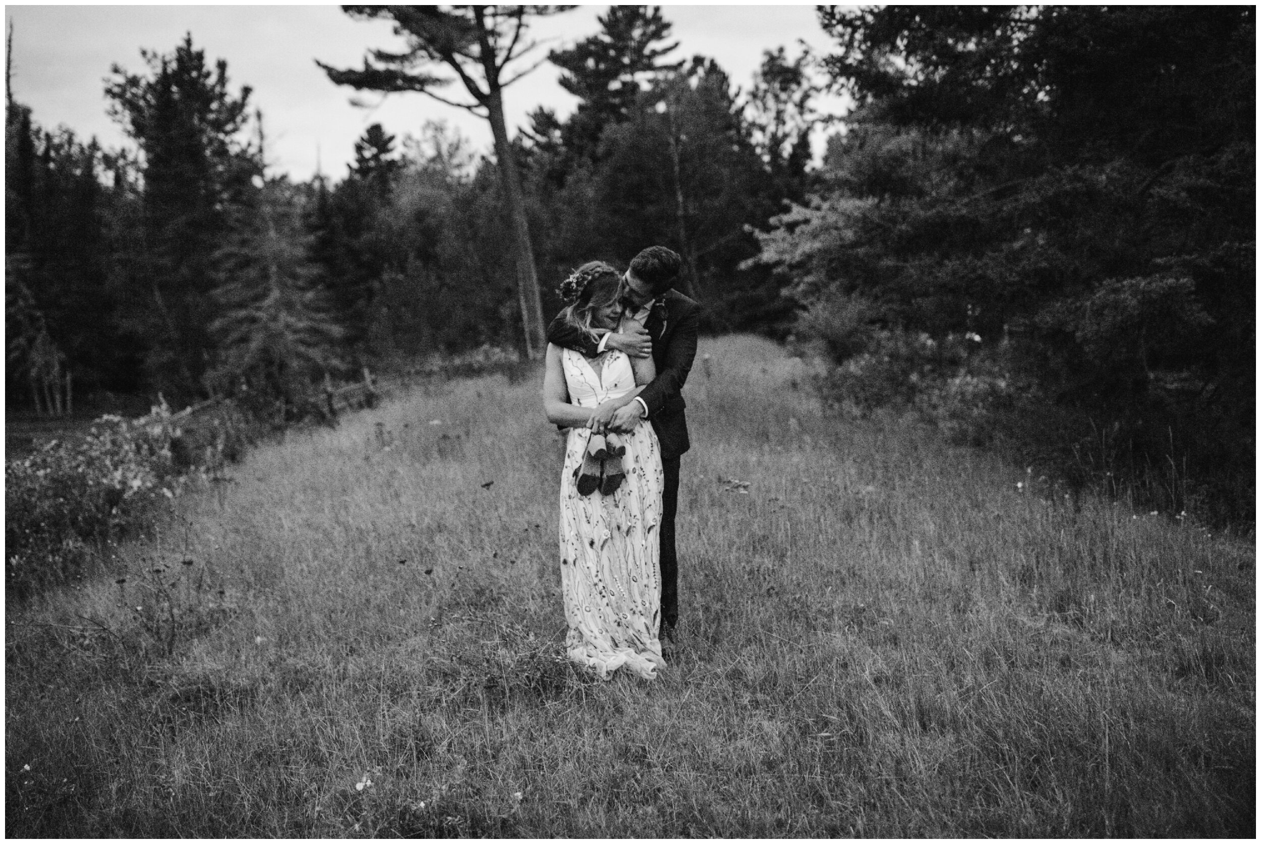 Groom hugging bride in wooded field at Minnesota summer camp wedding