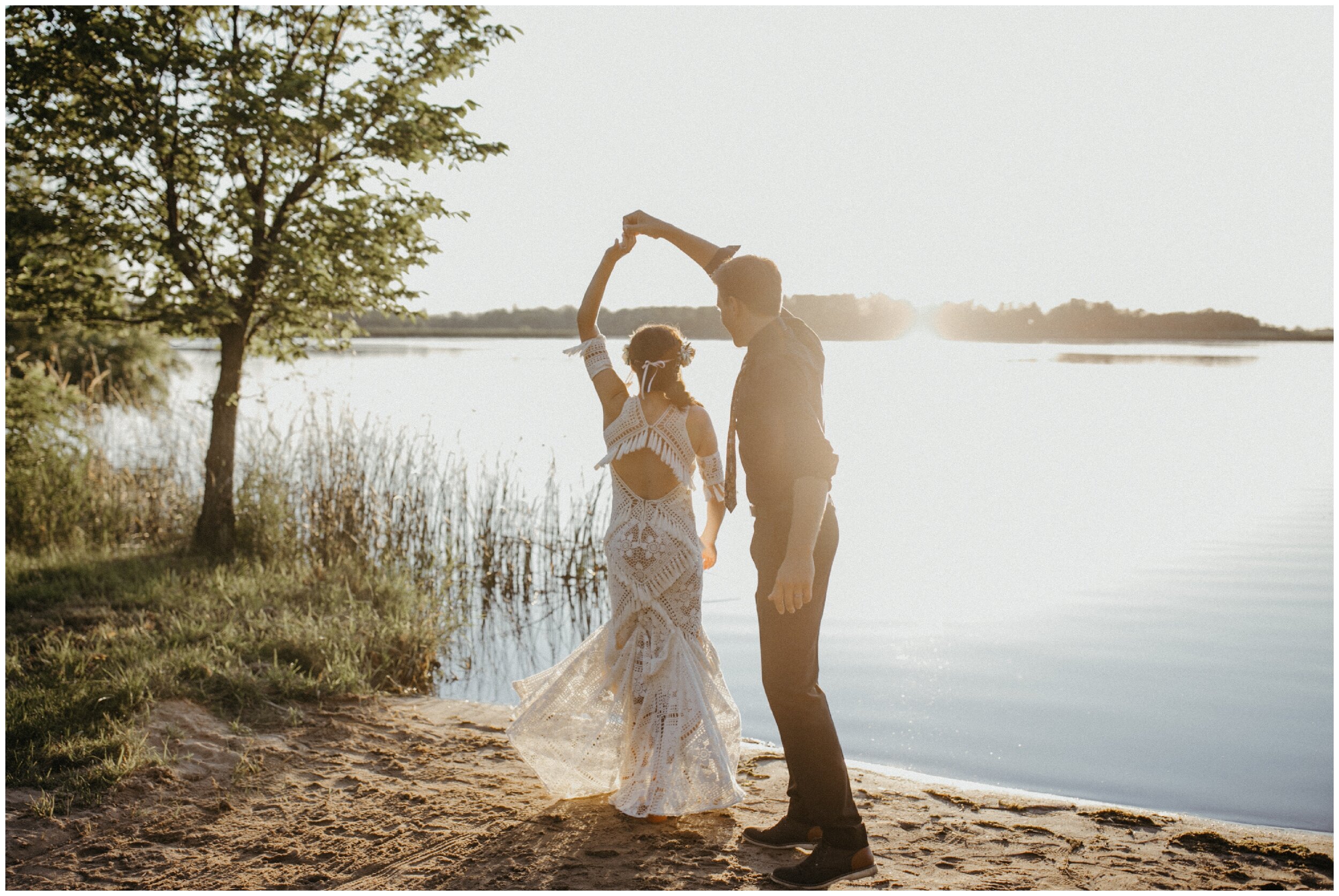 Groom spinning bride on lakeside beach during sunset at their Minnesota summer backyard wedding