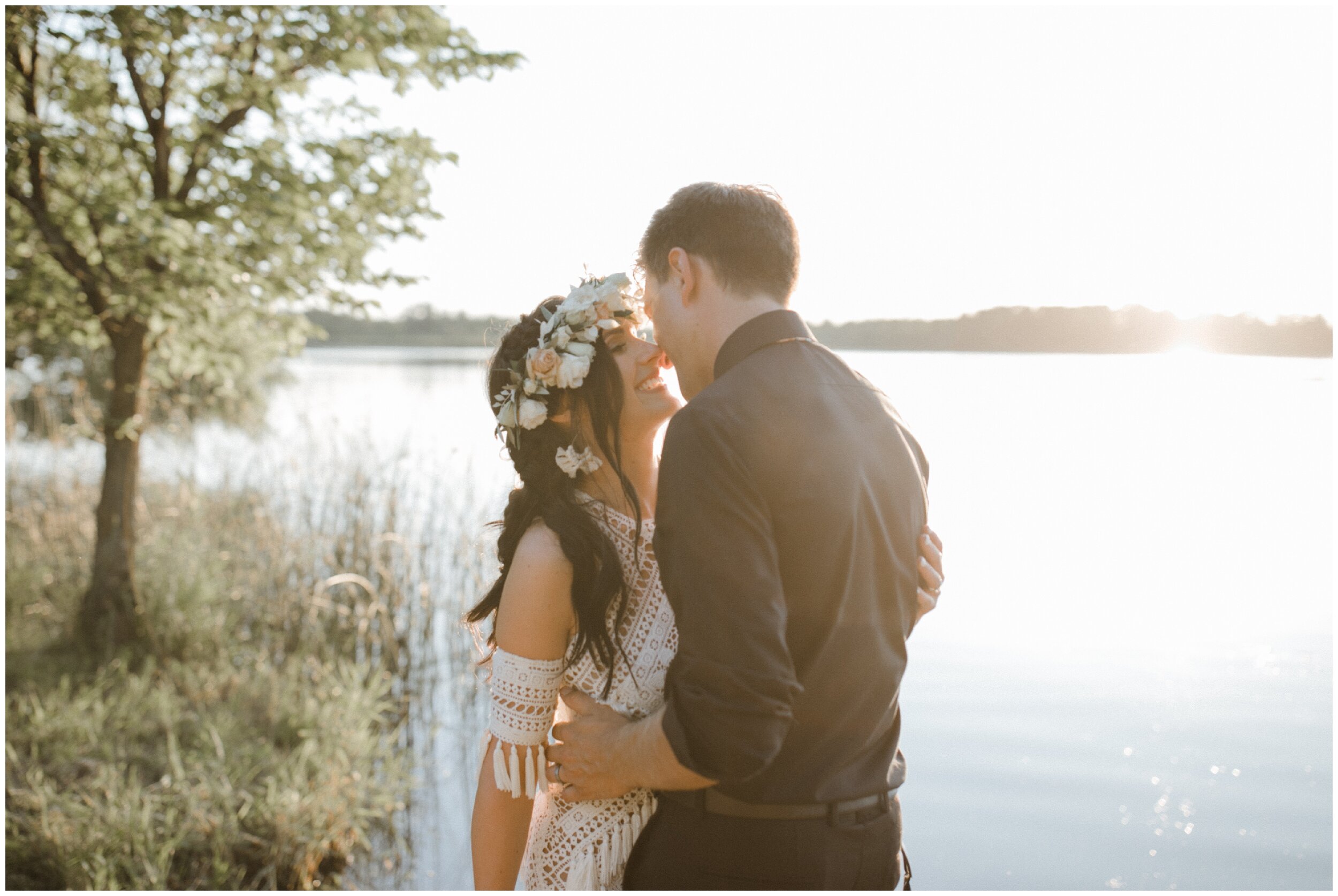 Bride and groom standing in front of lake during sunset at their Minnesota summer backyard wedding