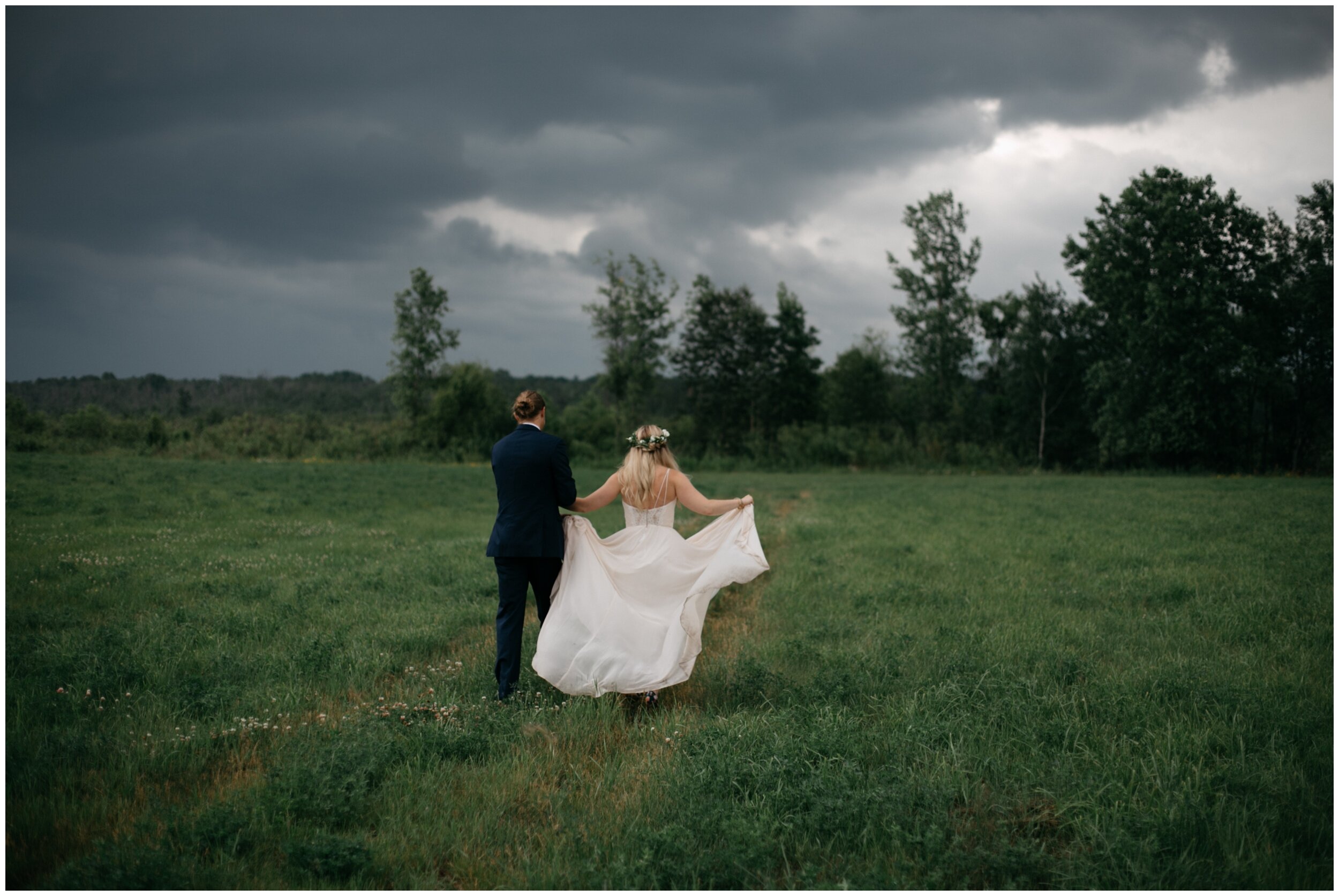 Bride and groom walking in field with stormy sky at the Northern Pacific Center wedding venue in Brainerd, Minnesota